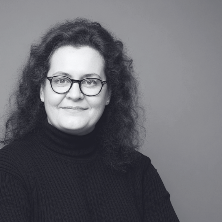 Cornelia Schmitz - Mentorin für Führungskräfte Porträt von Cornelia Schmitz. Eine freundlich lächelnde und Selbstvertrauen signalisierende Frau mit lockigem, dunklem Haar und Brille.